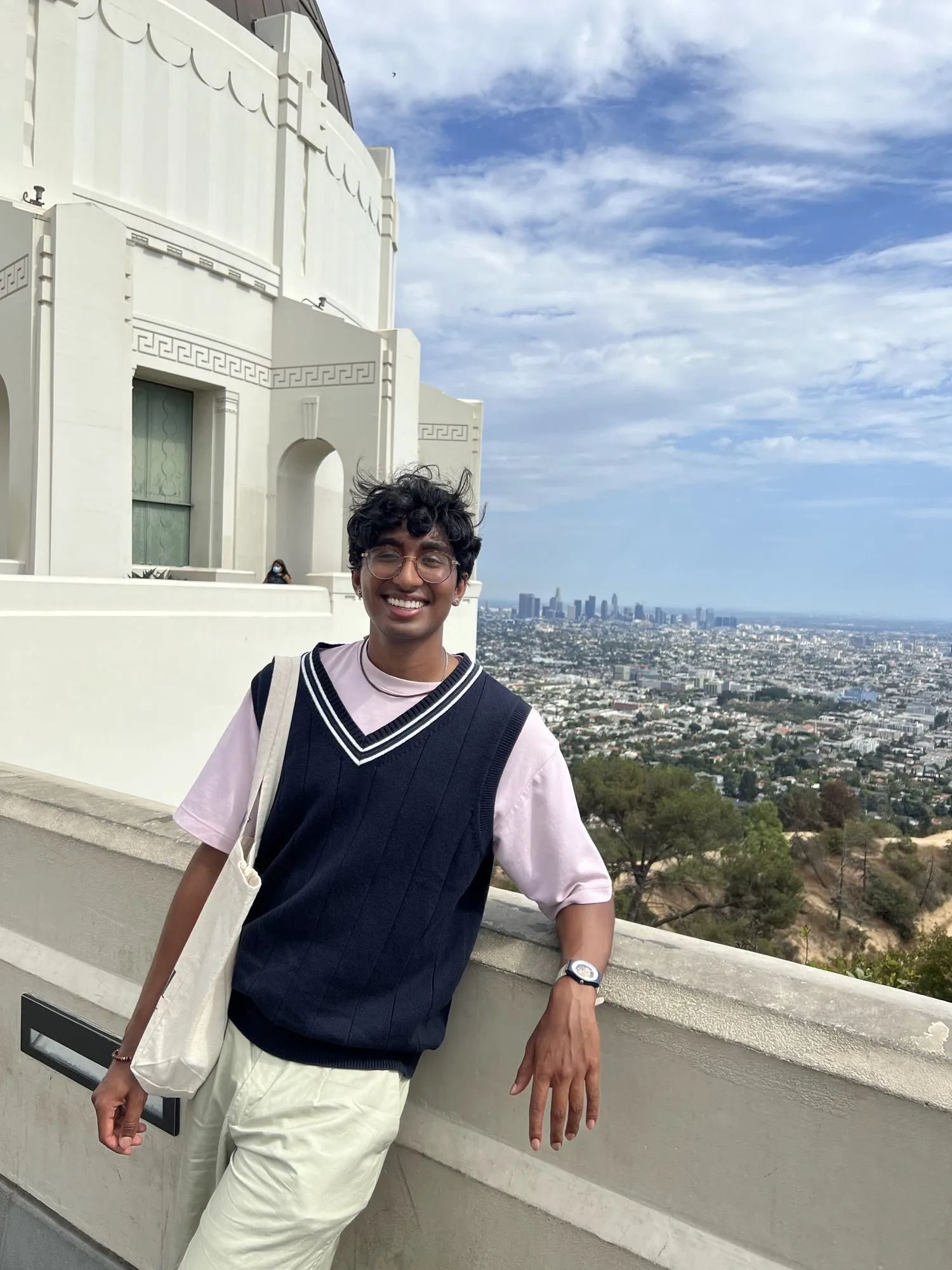 Adithya smiling, leaning on a white balustrade above Los Angeles under a blue sky.